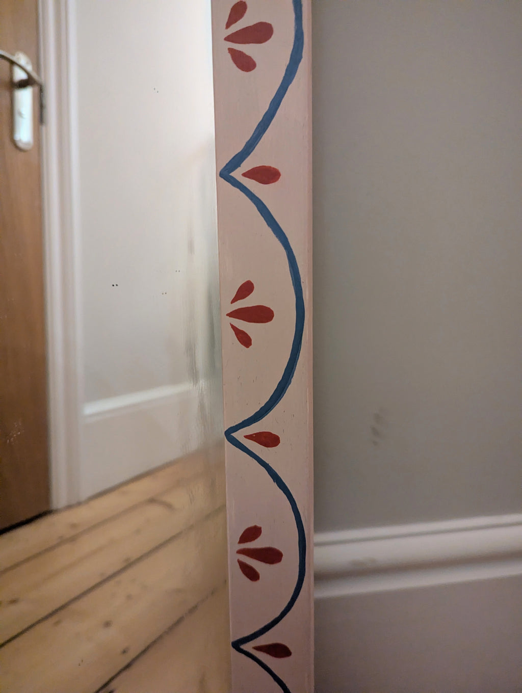 Pale pink mirror with whimsical red and blue pattern.